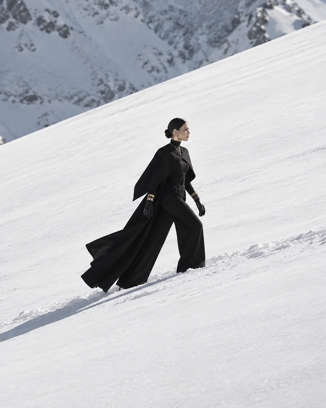 Model in black walking across a snowy mountainside